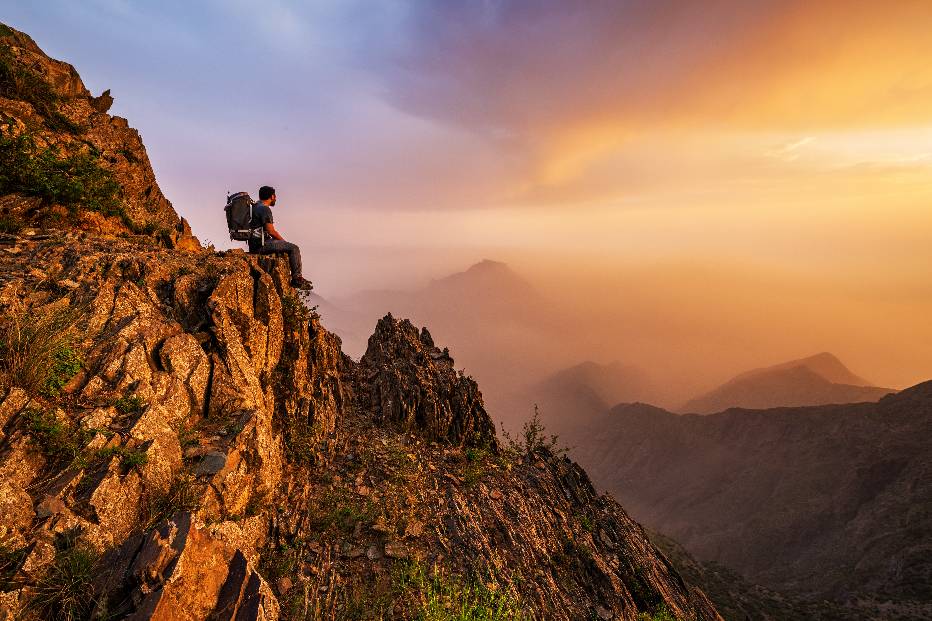 A person sitting on a rocky cliff Description automatically generated